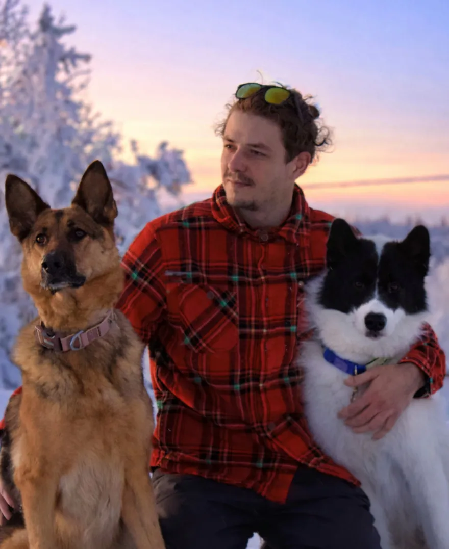 Dans la neige au couchant, un homme entre un berger allemand et un chien blanc à tête noire.